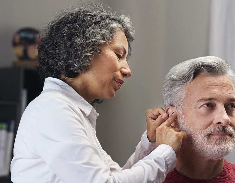 Audioprothésiste installant un appareil auditif dans l'oreille d'un patient malentendant