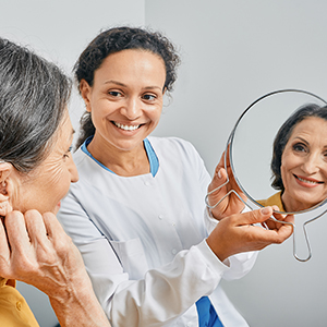 Audioprothésiste présentant un miroir à son patient pour qu'il puisse vérifier que son appareil auditif est suffisamment discret